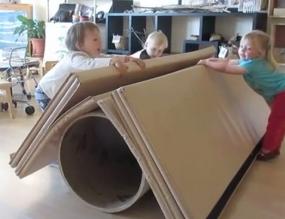 A group of two-year-old children work together to move a large folding gym mat thereby transforming it from a tent to a dance floor.