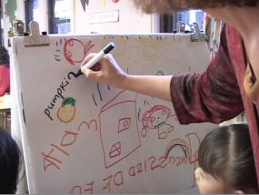 teacher writes words on bi-lingual preschool child's drawings